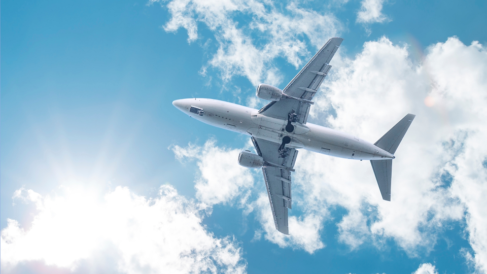 An airplane flies across the blue sky.