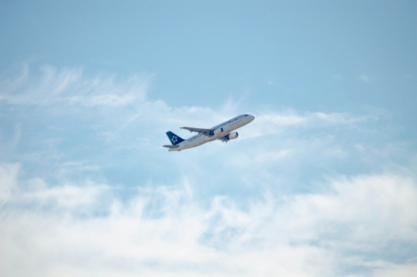 Commercial airplane taking off into a cloudy sky, viewed from behind as it climbs upward.