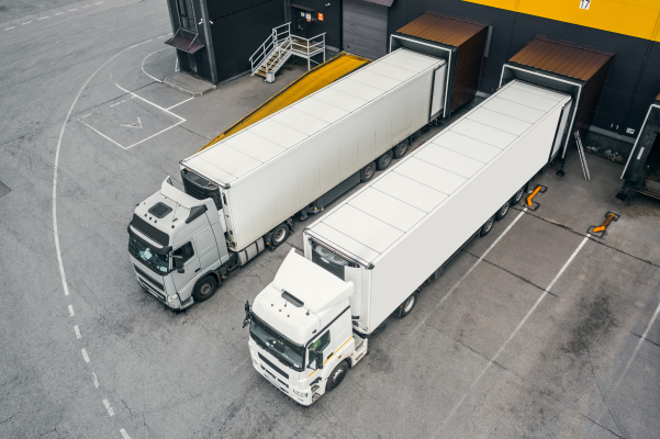 Two semi-trailer trucks backed into loading docks at a warehouse.
